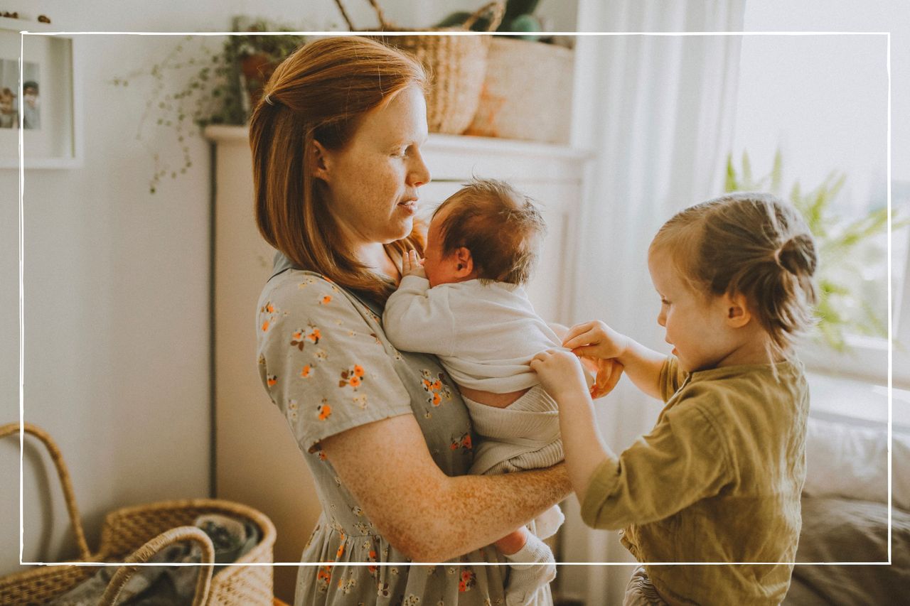 Mother holding young baby whole older child fixes baby&#039;s clothing