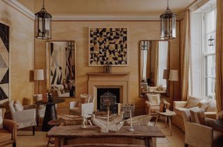 A drenched-in-beige hotel room features matching furniture items in sandy hues, including retro-fueled seating, crafty coffee tables, mirrors, and standing lamps.