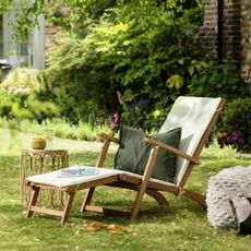Argos Home Folding Wooden Sun Lounger in a garden with a rattan side table and a green cushion