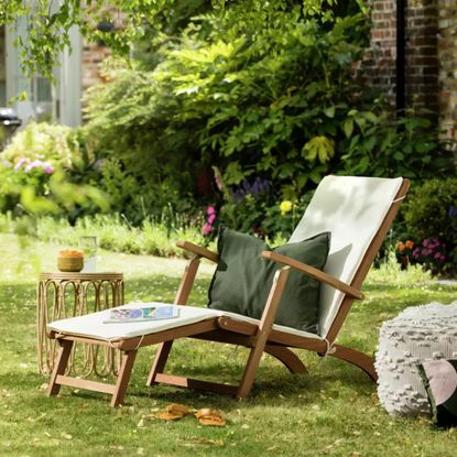 Argos Home Folding Wooden Sun Lounger in a garden with a rattan side table and a green cushion