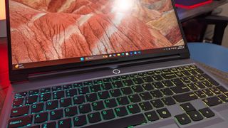 A Lenovo Legion 5i (Gen 9) gaming laptop open on a desk with a red backlight, showing the open display, RGB-lit keyboard, and white LED power button.