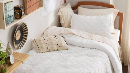 A white comforter on a twin bed against a wall beneath book shelves.