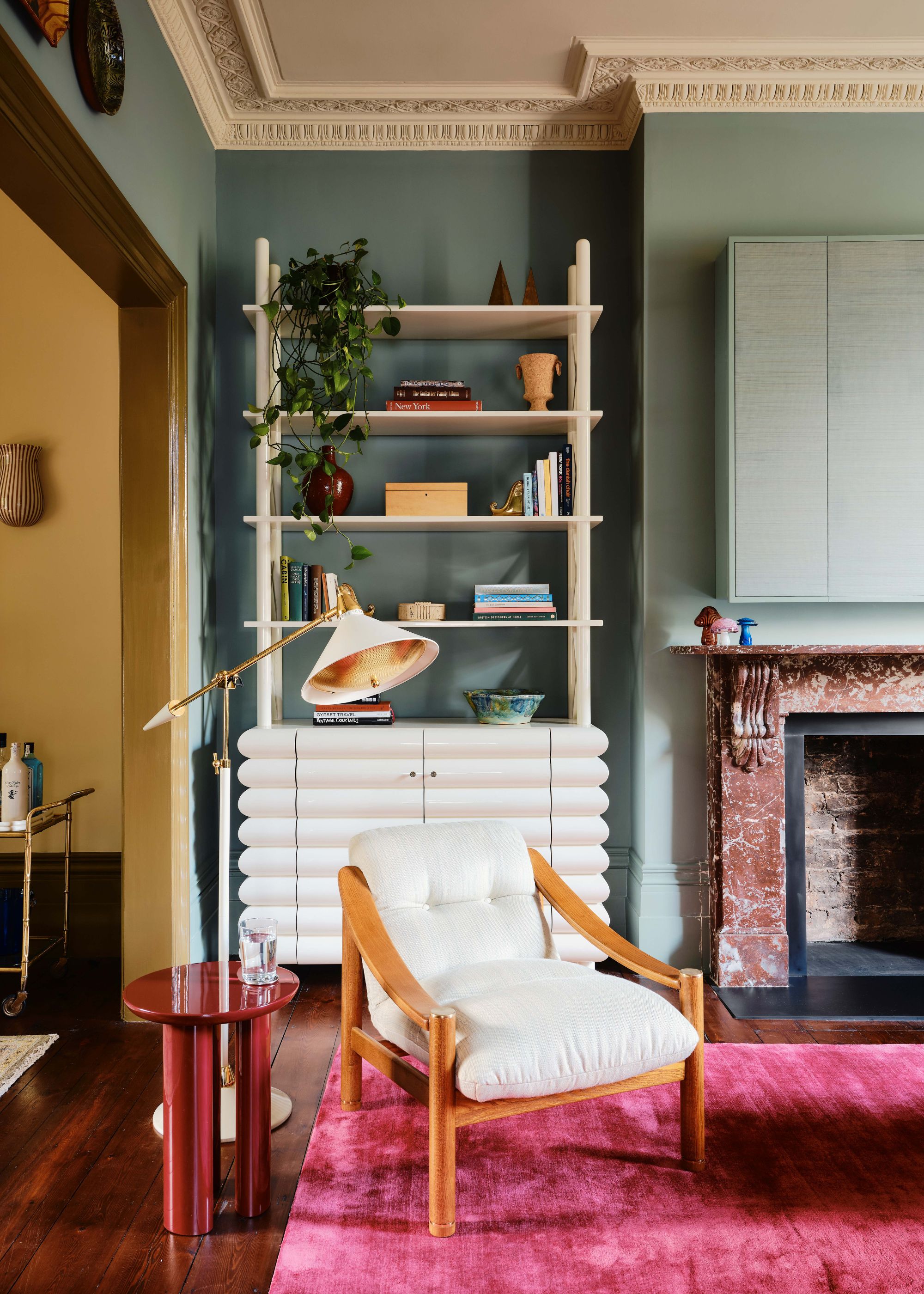 A colorful living room with teal walls, a hot pink rug, yellow walls in the adjoining room, and a white shelving unit.
