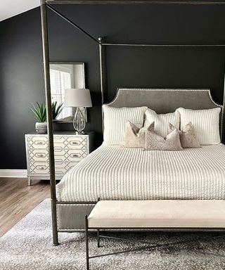 A canopy bed in front of a black accent wall