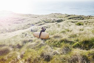 Woman walking across field with surfboard