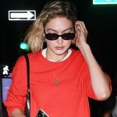 Gigi Hadid wearing a red oversized sweater, a long white maxi dress, and Adidas x Wales Bonner sneakers in New York City May 2024