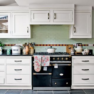 Black range cooker in a kitchen with white cabinets and green wall tiles