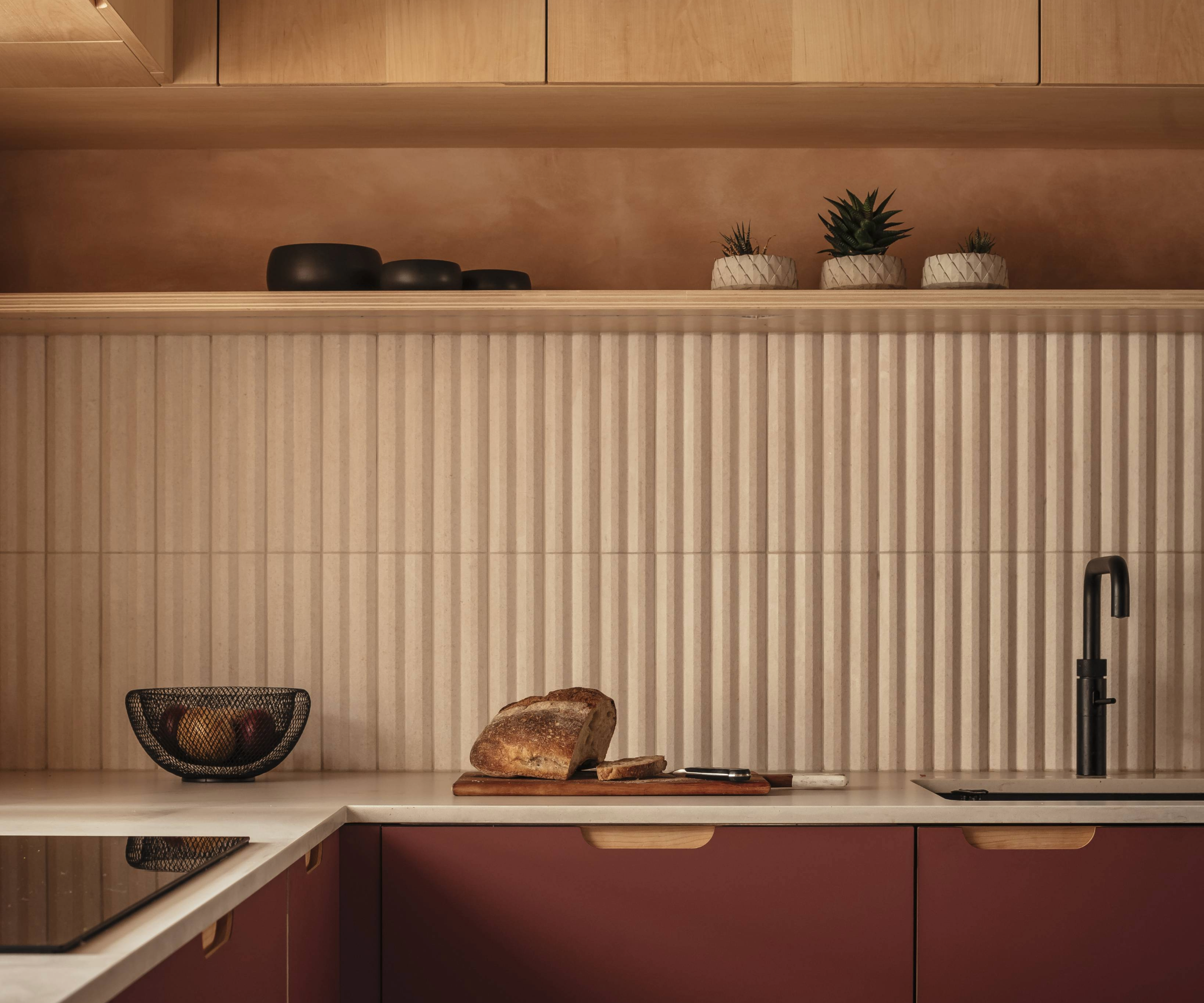 Close up of the burgundy worktops, fluted splash back and plywood cabinets with a loaf of bread on the worktop