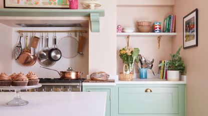 pastel green and pink Shaker kitchen with pink walls and green kitchen units and handing rail for pots and pans