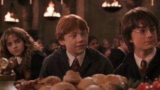 Emma Watson Rupert Grint and Daniel Radcliffe sitting at a table together in Harry Potter and the Chamber of Secrets.