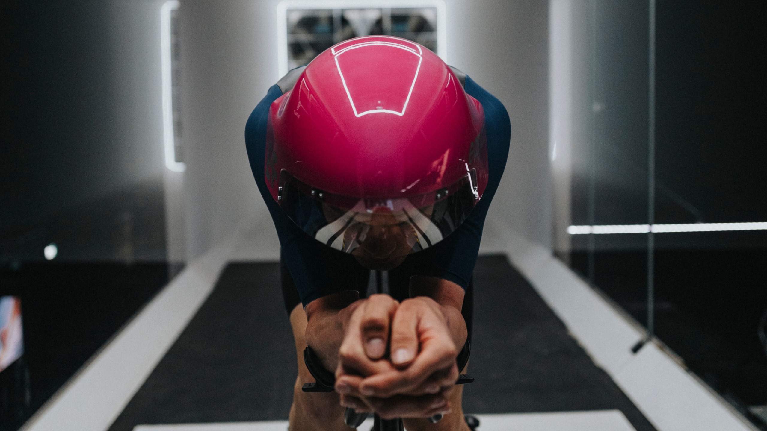 A rider in the wind tunnel wearing a cherry read POC Sonal helmet in an aggressive aerodynamic position 