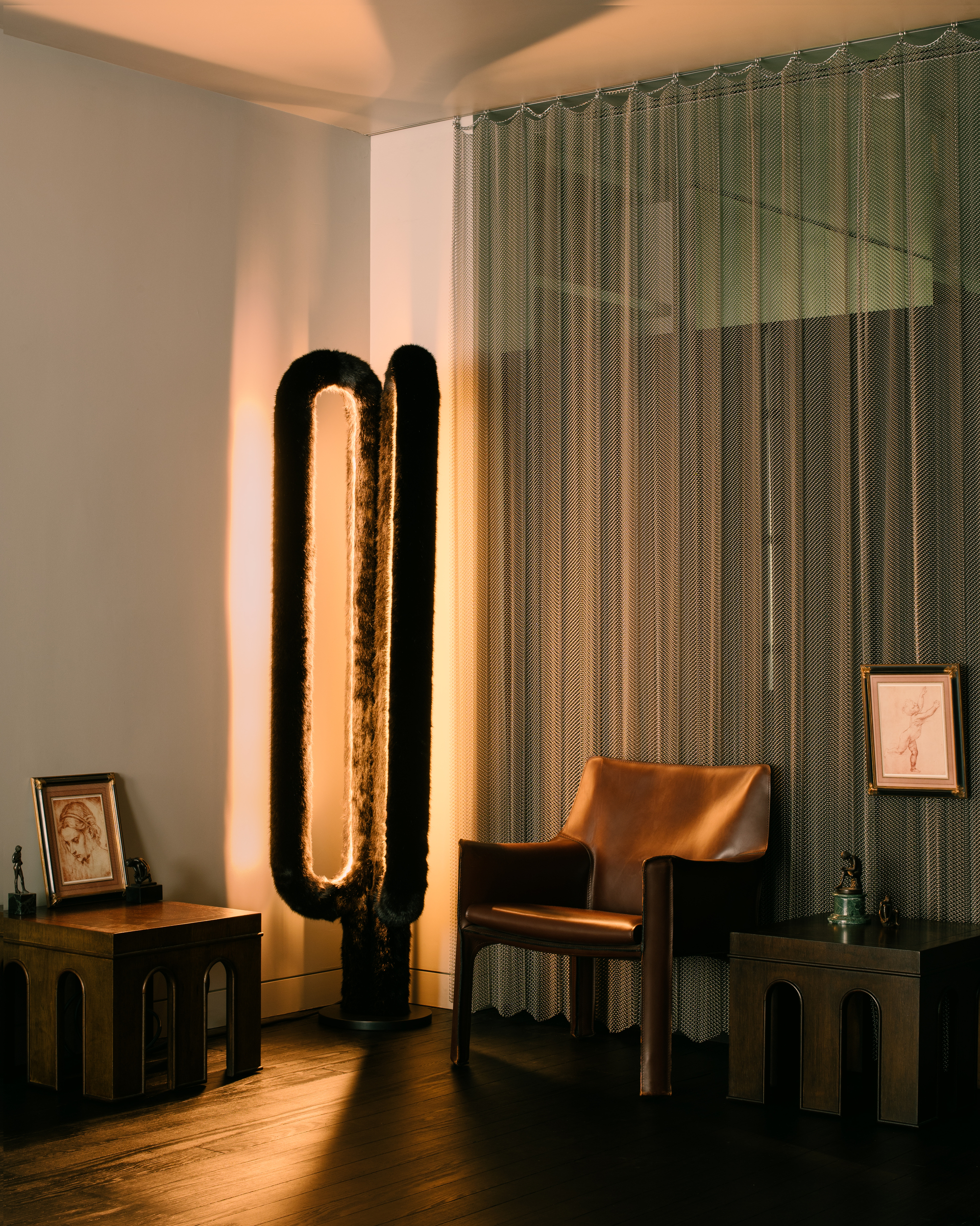 modern living room with sculptural floor lamp in the corner, a chain mail curtain screen, a side table with a framed picture on it, a leather chair next to another side table and a picture hanging from the chain mail