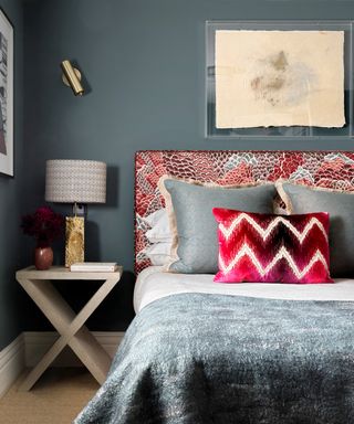 A bedroom with a blue wall behind a bed with a red, white and blue patterned headboard and complementary cushions and bedding