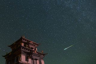 A large building on the left and a bright green white perseid meteor streaking across the star filled sky.
