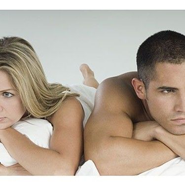Man and woman lying on white bedsheets, looking disappointed
