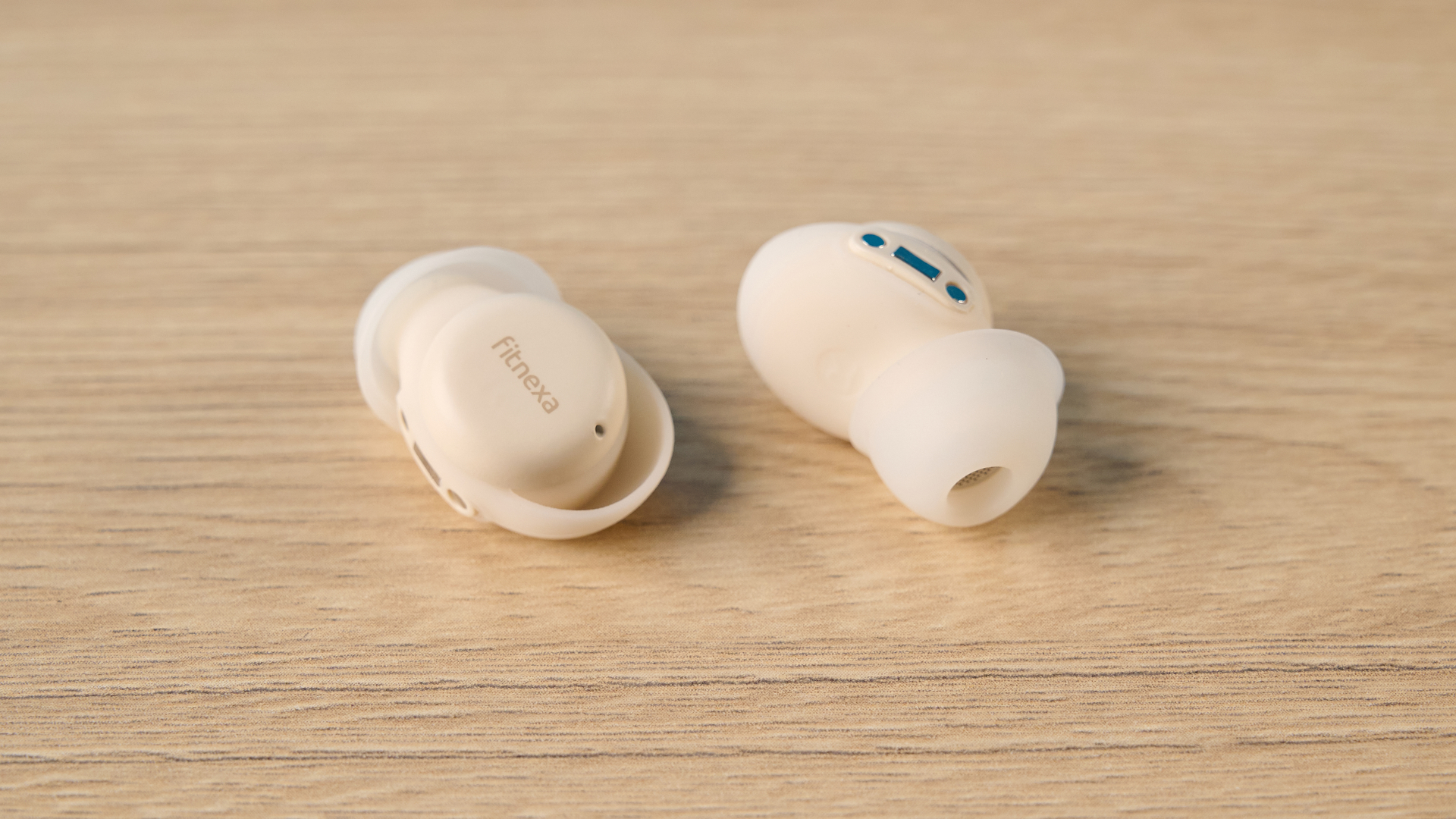 A closeup of the Fitnexa SomniPods 3, one facing toward the camera and one away, on a wooden table