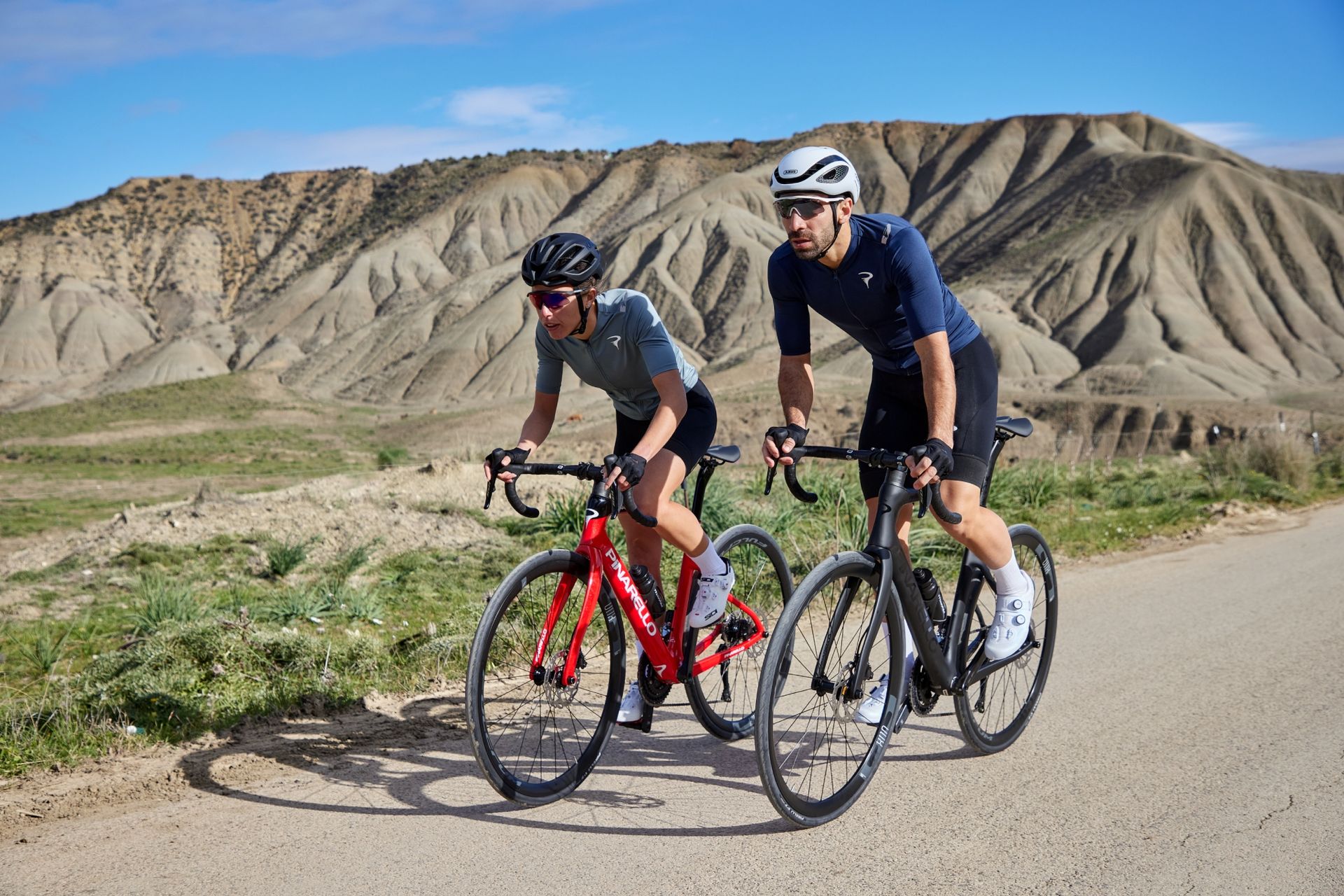 A male and female cyclist riding Pinarello X road bikes with mountains in the background