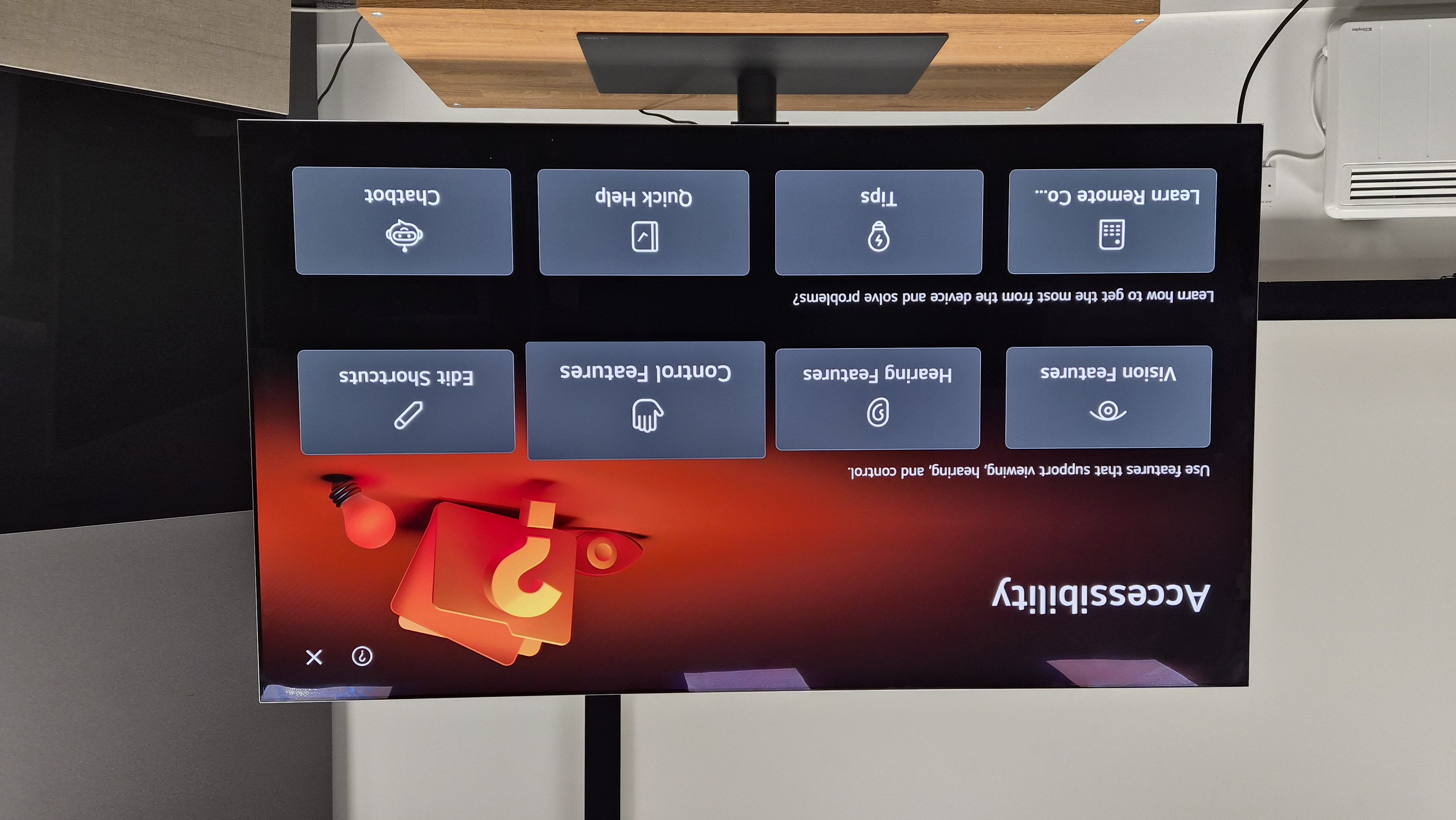 Image of an Accessibility screen on an LG G5 TV. There are 8 different drop downs. These are Vision Features, Hearing Features, Control Features, Edit Shortcuts, Learn Remote Control, Tips, Quickhelp and Chatbot. This is all on a black background, with an orange hue in the top right corner, featuring a graphic of a question mark.