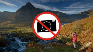 'No photogaphy' sign in the middle of mountain landscape with photographer taking a photo in the foreground 