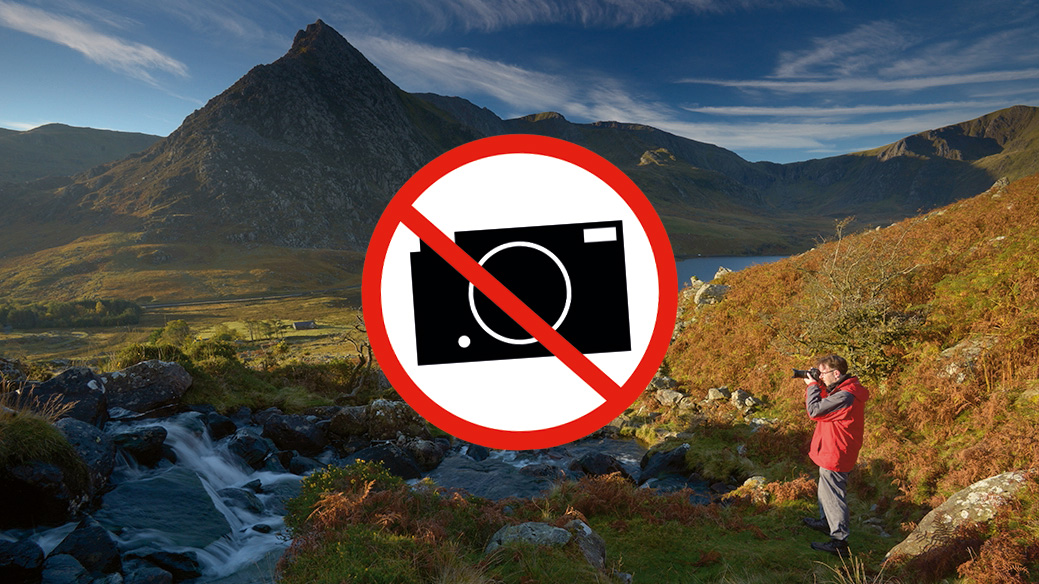&#039;No photogaphy&#039; sign in the middle of mountain landscape with photographer taking a photo in the foreground 