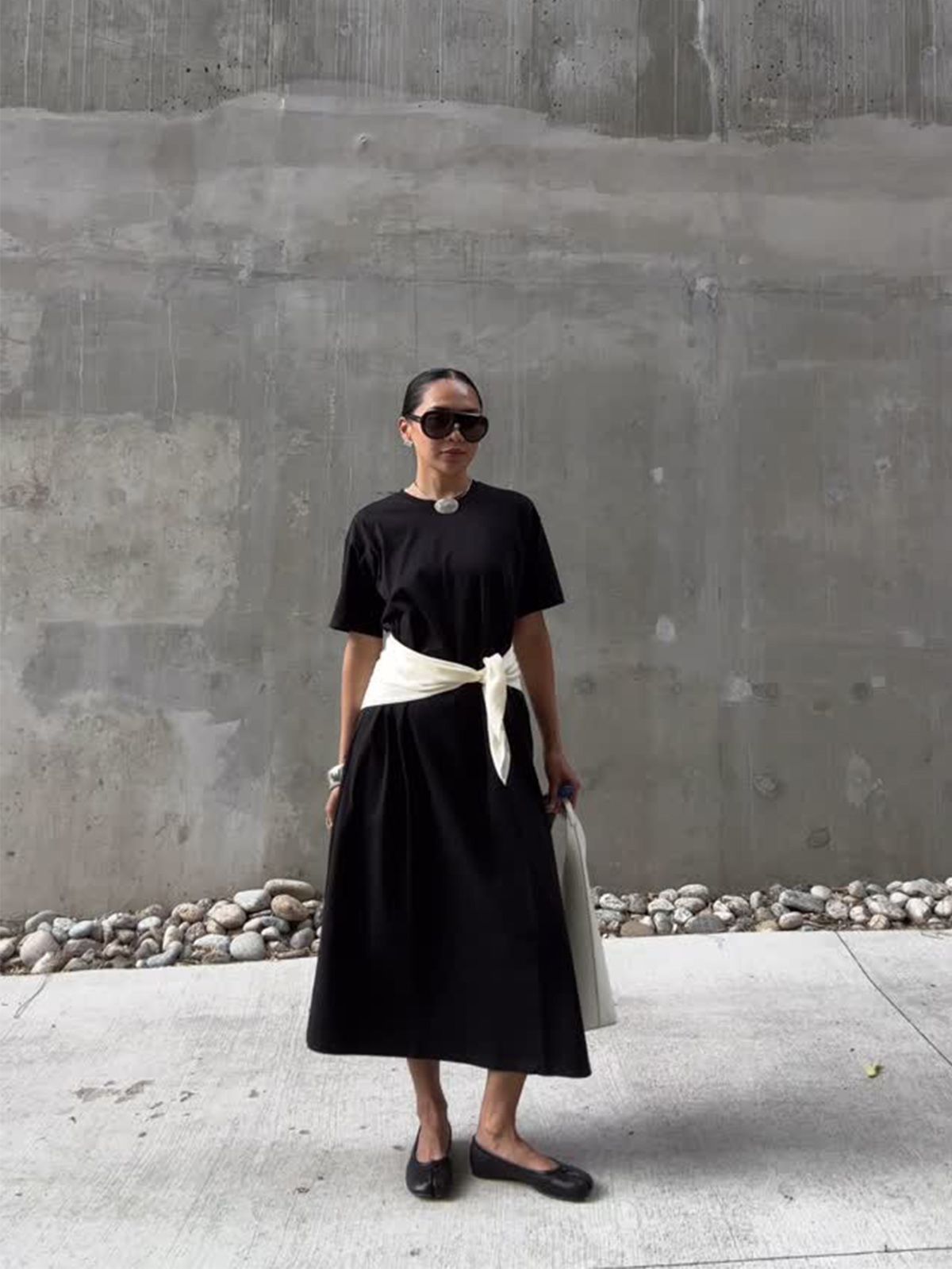 @dawn.tan wearing a black T-shirt dress with a white sweater around waist and ballet flats.