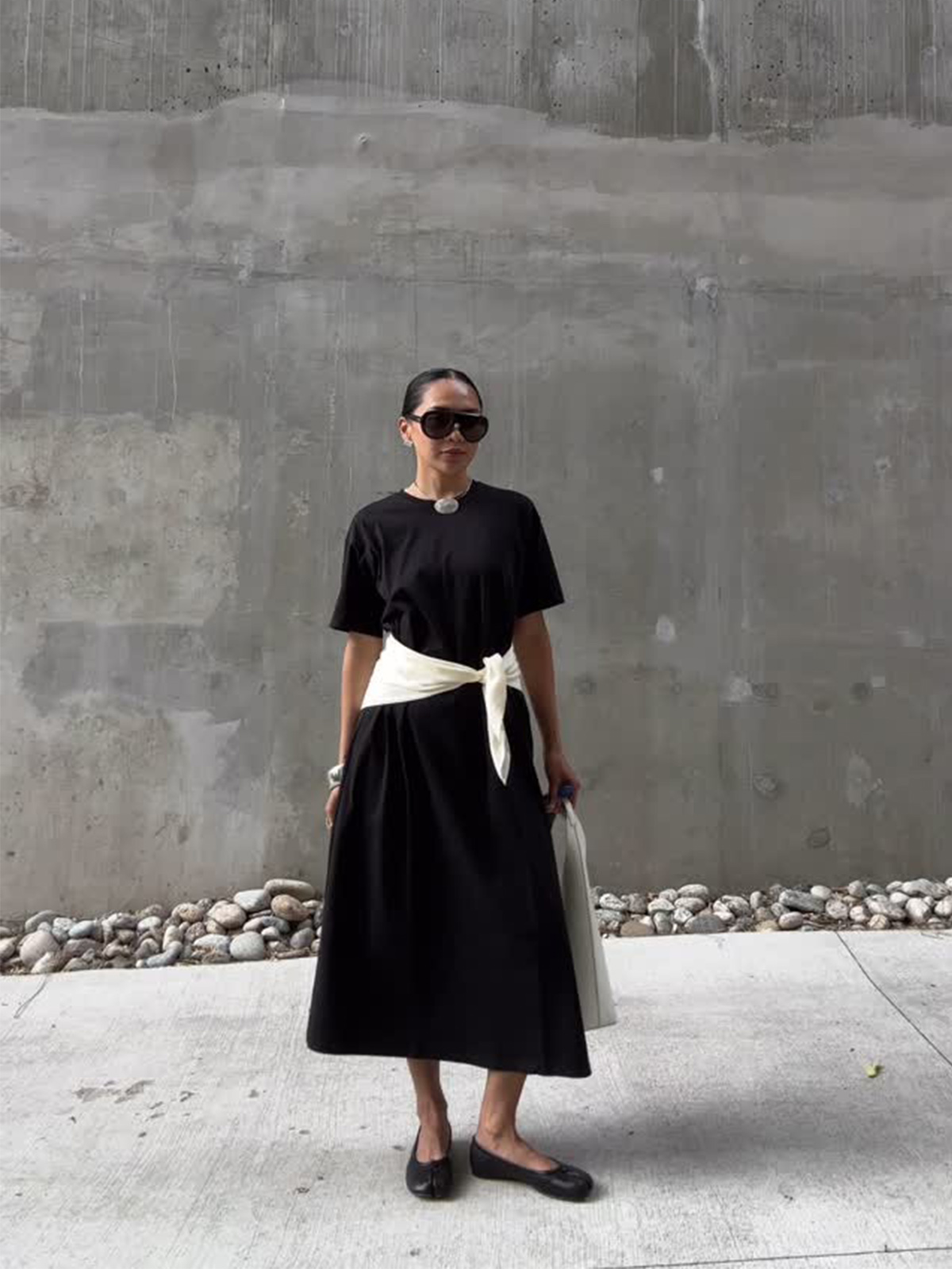 @dawn.tan wearing a black T-shirt dress with a white sweater around waist and ballet flats.