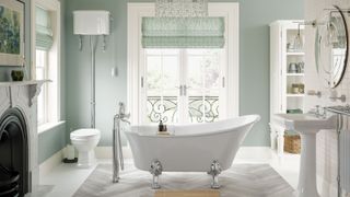 white roll top bath in bathroom with window, black and white fireplace, pale green walls and vintage style sink and toilet