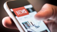 Close up of hand holding smartphone showing news web page