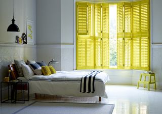 Yellow shutters in very plain white bedroom