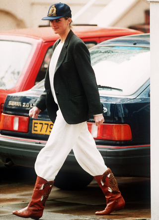 Princess Diana wearing an unusual combination of white trousers, boots, a blazer jacket and a baseball cap after taking her sons to school at Wetherby, 25th April 1989