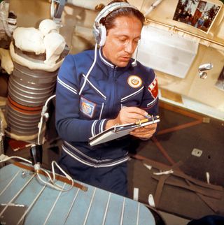 photo of a man in a blue flight suit holding a pencil and a clipboard
