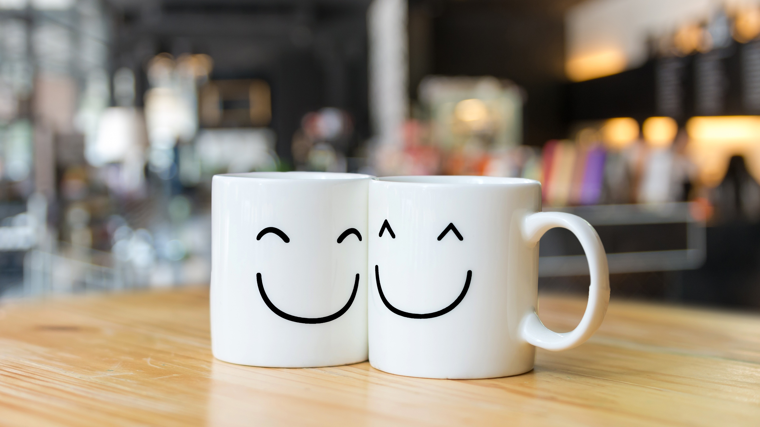 Two coffee cups with smiley faces sitting close together on a cafe table.