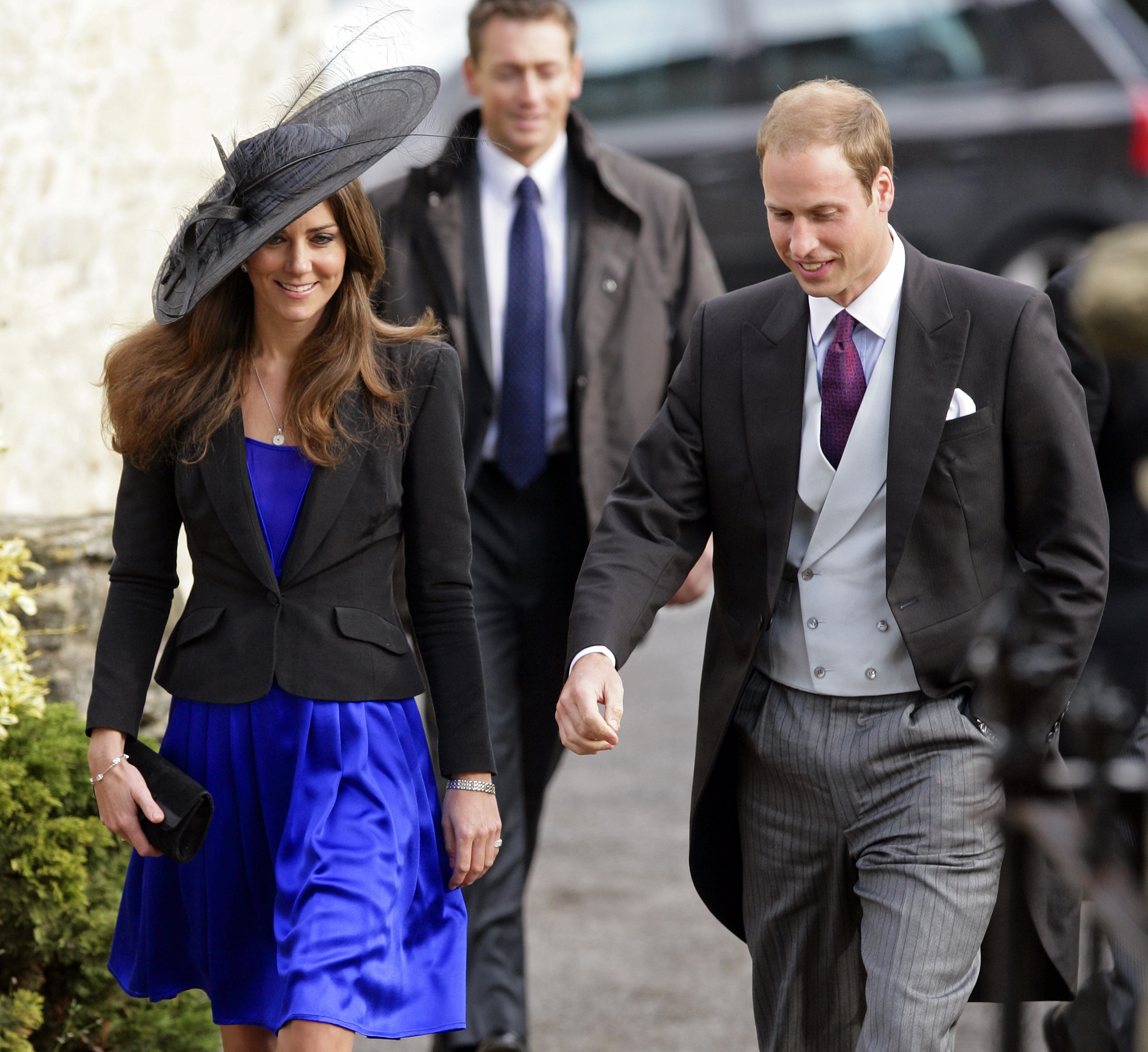 Kate Middleton wears a royal blue dress and a black jacket and hat while attending a wedding with Prince William in October 2010