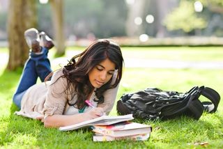 A woman studies on the lawn of a college campus.