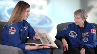 Canadian Space Agency (CSA) astronaut Jenni-Sidey Gibbons (left) shows a scrapbook to Roberta Bondar, a retired CSA astronaut. Sidey-Gibbons, when a small child, created the scrapbook in 1992 to follow coverage of Bondar's mission when Bondar became the first Canadian female astronaut in space.