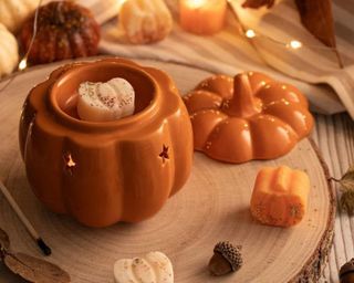 An orange pumpkin wax melt on top of a wooden board with pumpkin wax melts around it