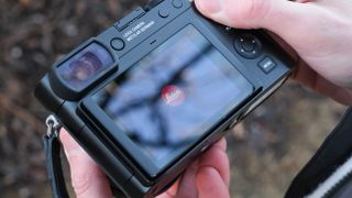 The back of a Leica Q3 43 camera with the screen displaying the Leica logo, held in a person's hands