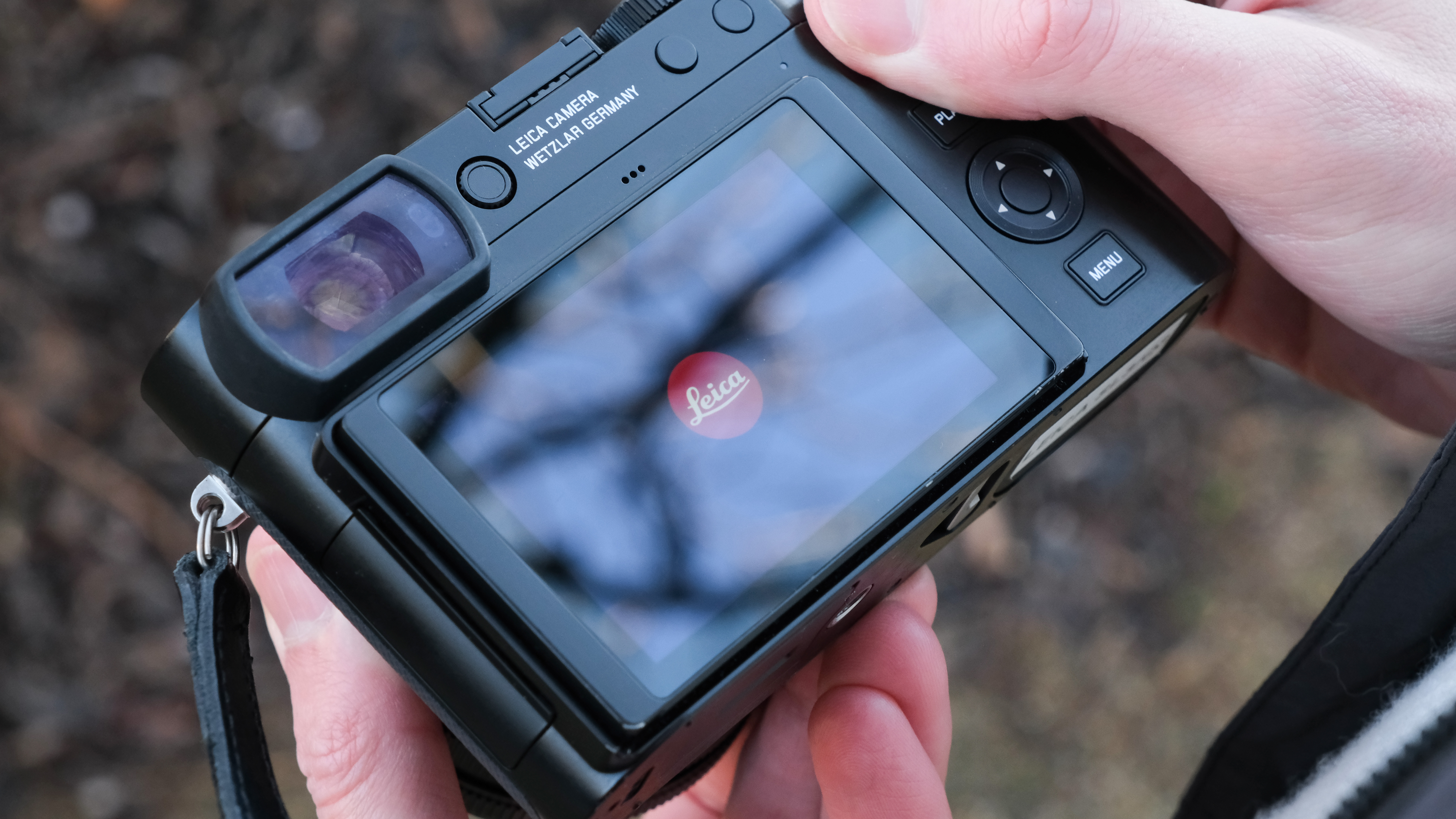 The back of a Leica Q3 43 camera with the screen displaying the Leica logo, held in a person&#039;s hands