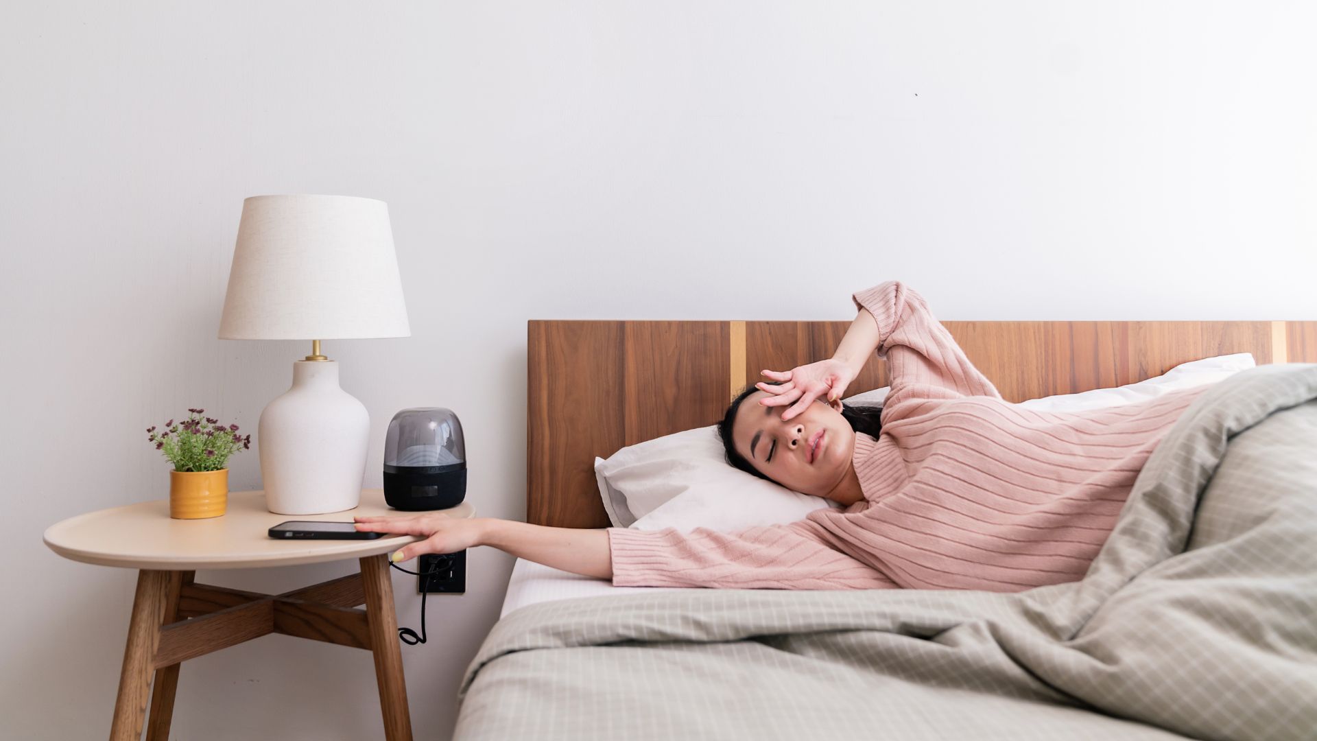 A woman wakes up in the morning, looking tired, and reaching for her phone with one hand to see how much she has overslept on the weekend compared to the time she normally gets up for work each day.