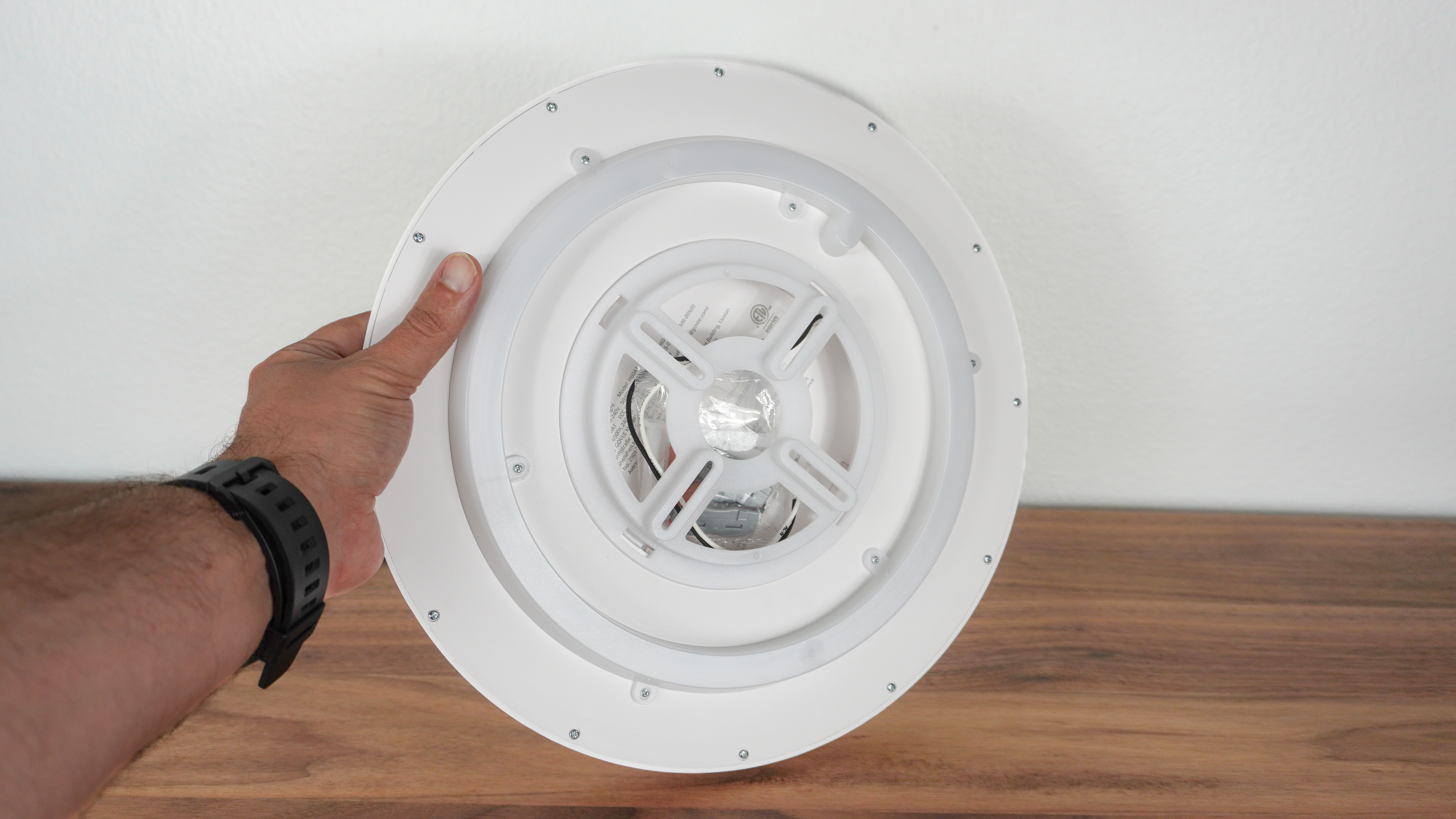 A person holding Govee's smart ceiling light with all of the installation hardware tucked into the back of the light