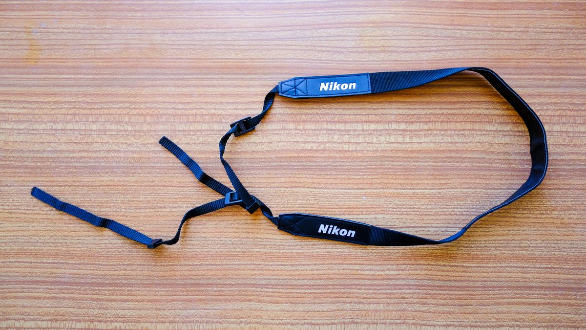 The neck strap for the Nikon Action 16x50 binoculars on a wooden table.