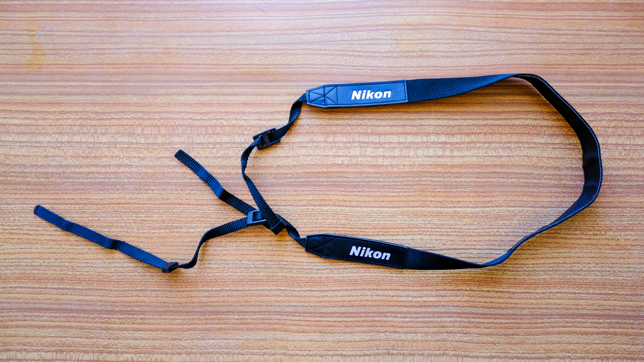 The neck strap for the Nikon Action 16x50 binoculars on a wooden table.