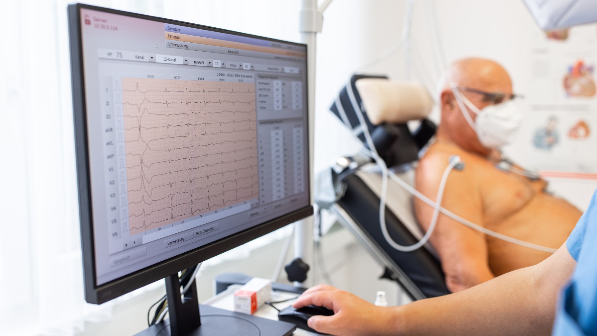 Computermonitor mit EKG-Herzbelastungstestergebnissen eines älteren männlichen Patienten auf einem Fahrrad.  Nahaufnahme des Computerbildschirms in der Kardiologieklinik.