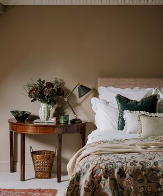 The Alana Square Cushion on a bed against a beige wall.