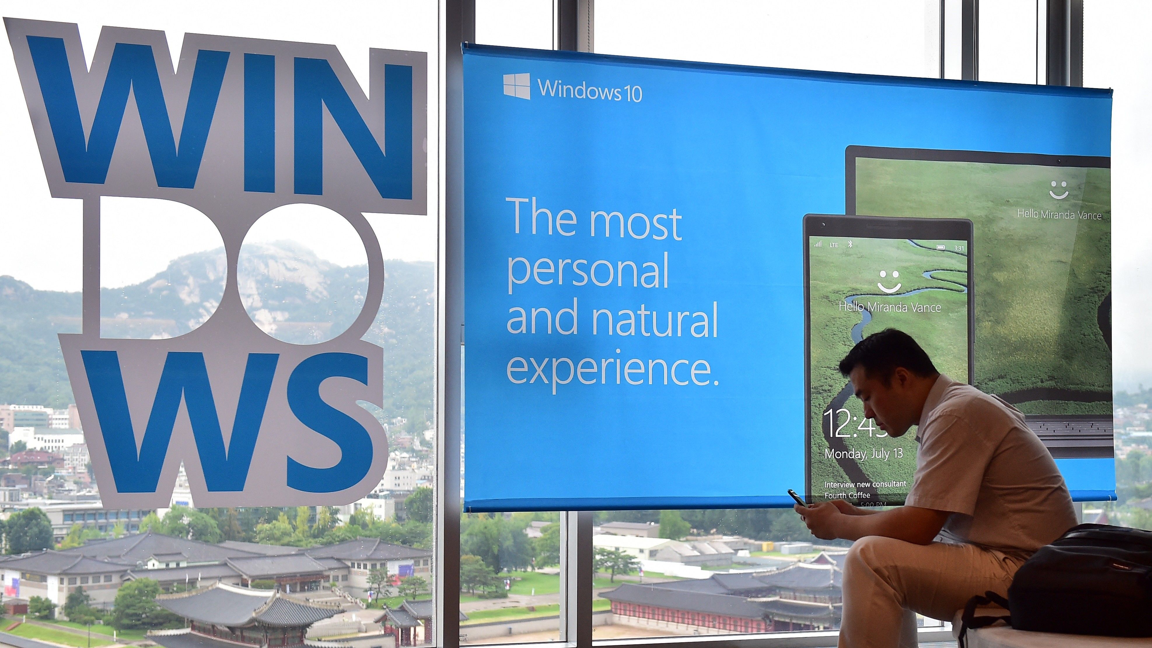 A man sits in front of a billboard for Windows 10, the latest operating system from US software giant Microsoft, during a launch event in Seoul on July 29, 2015.