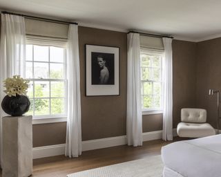 A bedroom with brown suede walls, white armchair and black table lamp on white side table
