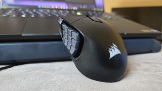 A Corsair Scimitar Elite Wireless SE gaming mouse on a carpet next to a gaming laptop and Stream Deck.