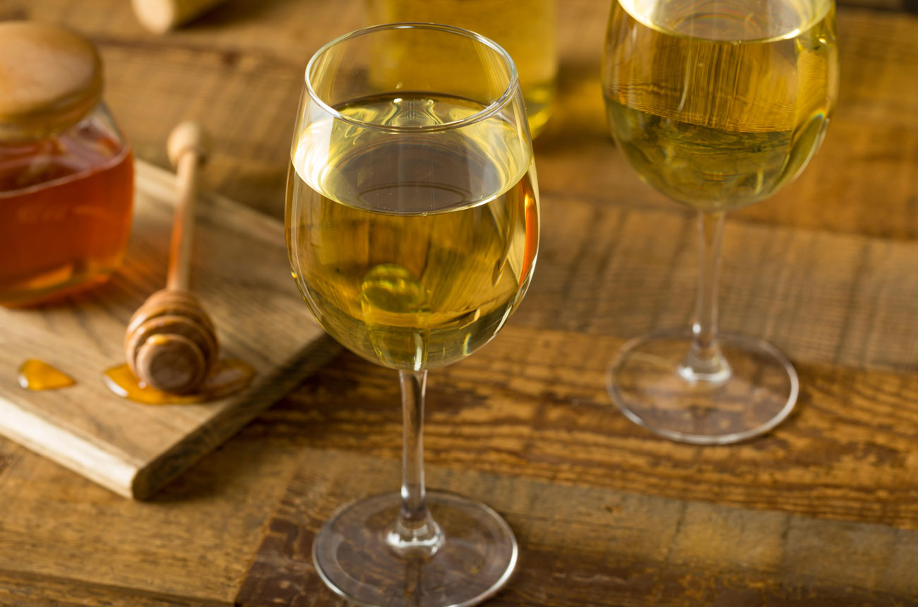Two glasses of mead with honey jar in background