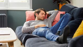 A man in a grey top takes a power nap on his couch to get over jet lag