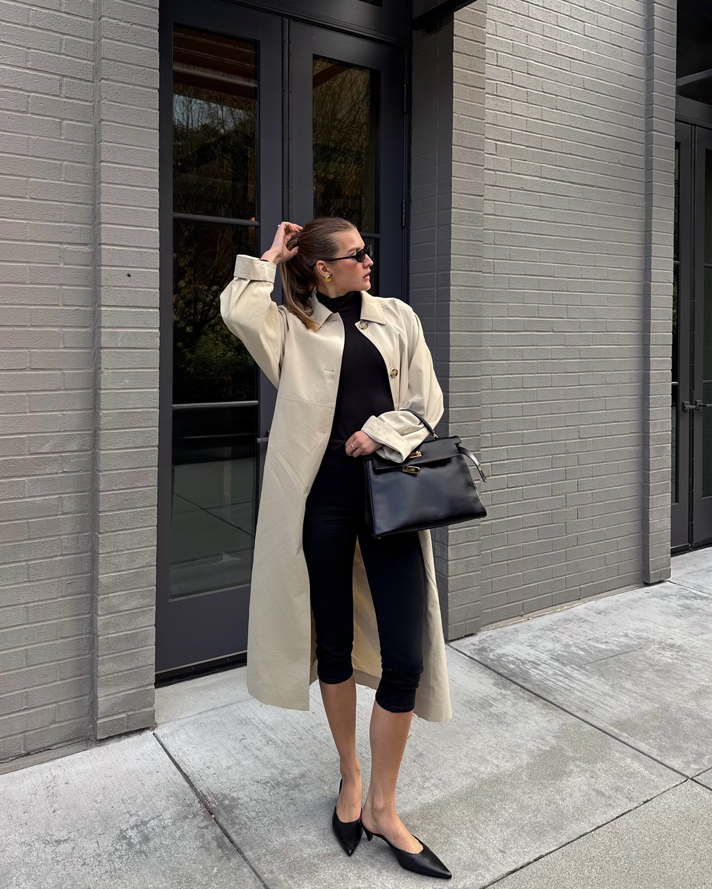 Sara Walker wearing a tan trench coat over an all black outfit.